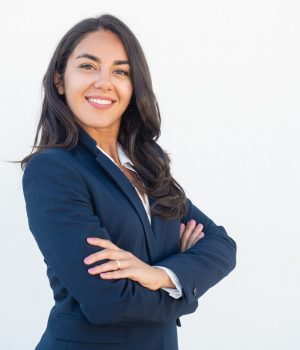 Smiling confident businesswoman posing with arms folded. Happy beautiful black haired young Latin woman in formal suit standing for camera over white studio background. Corporate portrait concept
